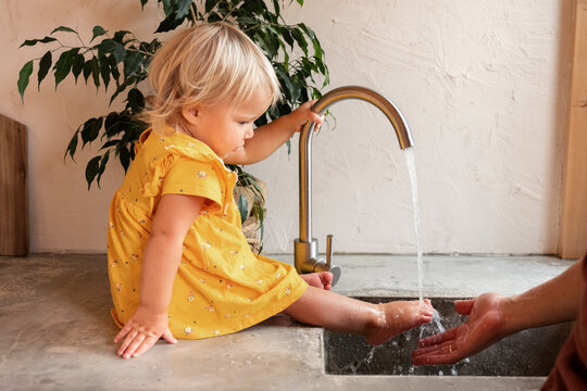 Crop parent washing foot of toddler over sink