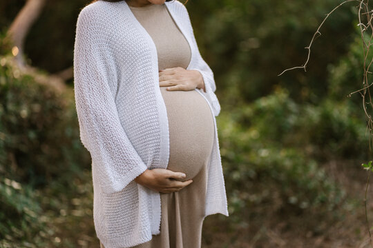 Pregnant woman tenderly embracing belly in nature