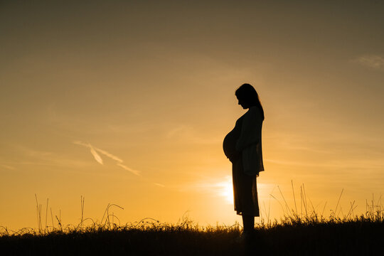 Unrecognizable pregnant woman at sunset time