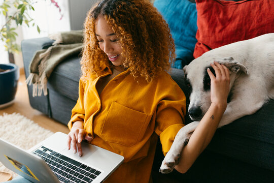 Pretty curly haired girl at home with dog and laptop