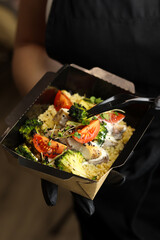 Healthy bowl with bulgur, broccoli, chicken in cream sauce, greens and tomatoes with plastic fork in the hands of the chef. Healthy food delivery service and daily ration concept.