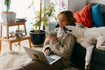 Girl smiling using laptop and drinking coffee with dog