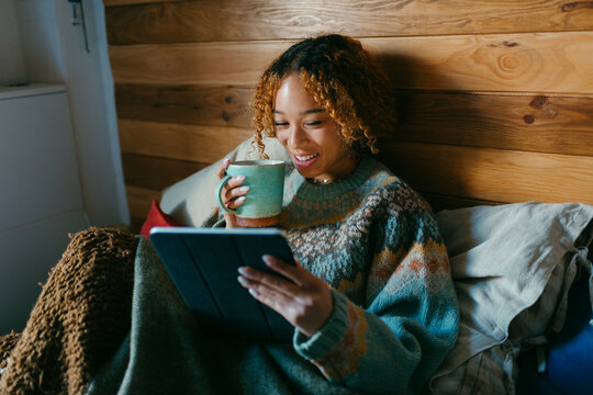 Teenager in cozy bedroom using tablet and drinking tea