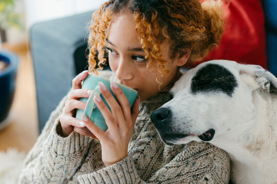 Teenager at home bonding with dog while drinking tea
