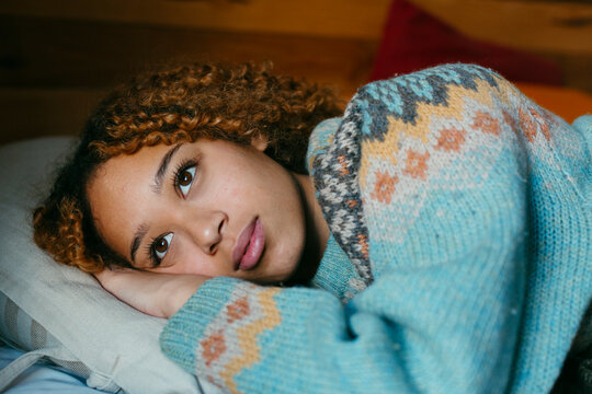 Young woman lying on bed in winter clothes looking sad