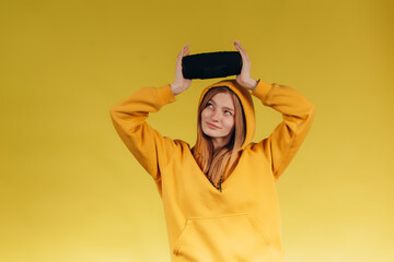 Funny young girl looking, waving hand, holding portable wireless bluetooth music speaker, isolated...