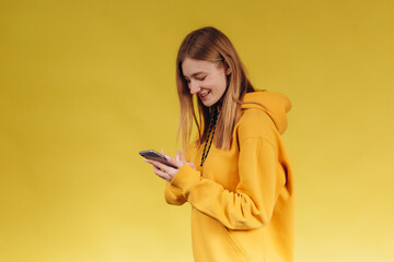 Portrait of a young teen girl holding a phone, a girl talking on the phone, wearing a casual yellow hoodie in one tone with the background