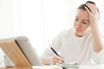 Young woman studying online with tablet or laptop and writing down notes. Online education for young people at home - studying on a distance via internet