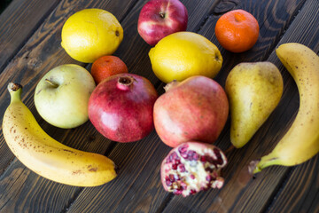 Pomegranates, lemons, bananas, apples, tangerines and pear on a table of wooden planks.