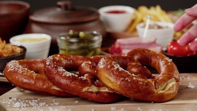 Putting fresh baked pretzel close-up. Traditional German Cuisine. Smoked sausages with fried potatoes, pickled cucumbers, bratwursts on table. Composition of Cooked National Czech Food. 