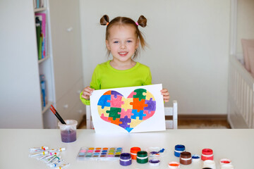 A two-year-old girl shows her drawing in support of children with syndrome autism. The child drew a...