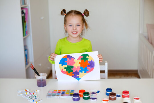 A two-year-old girl shows her drawing in support of children with syndrome autism. The child drew a picture of a heart from colorful puzzles. Teach children to be tolerant and support special people