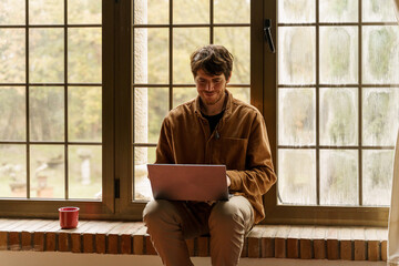 Portrait of man sitting by the window using laptop