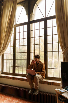 Portrait of man sitting by the window using laptop