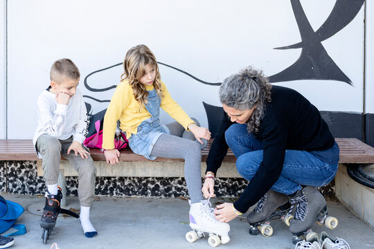 Mother tying skates of daughter and son in park