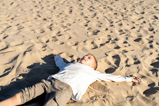 Cheerful kid lying on sandy seashore in sunlight