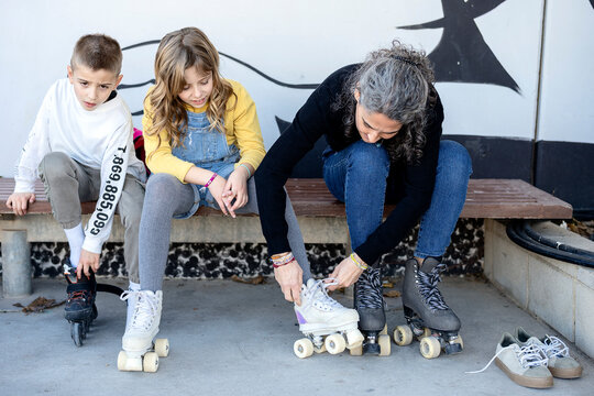 Adult woman helping children to wear roller skates