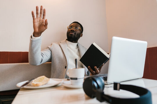 Black man with book calling waiter in cafe