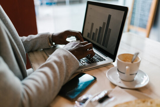 Anonymous black worker typing on laptop in cafe