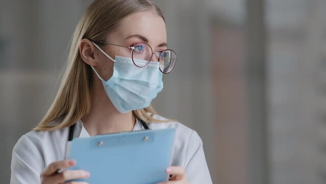 Portrait caucasian woman doctor nurse in medical protective mask writing information in medical registration journal female in glasses therapist working clinic hospital handwriting notes appointment