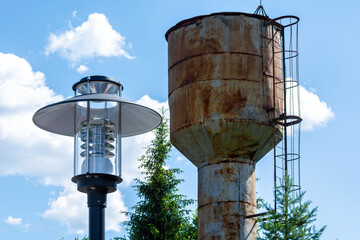 Street lamp and an old rusty water tower against a blue sky.