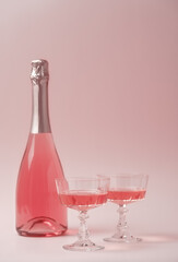 Two crystal glasses and bottle of rose sparkling wine or champagne on pastel pink background....