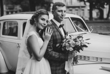 Happy young newlyweds bride and groom standing near a retro auto. Black and white