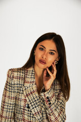 a brunette girl poses on a white background in a beige jacket and black trousers