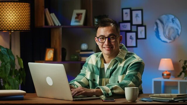 Asian man portrait, typing on laptop, sitting in living room. Korean young guy working remotely at home during coronavirus lockdown. Businessman using computer for remote work, freelance. 