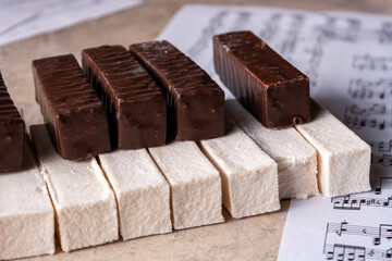 A piano keyboard made of white and chocolate marshmallows lies on music paper, selective focus, close-up