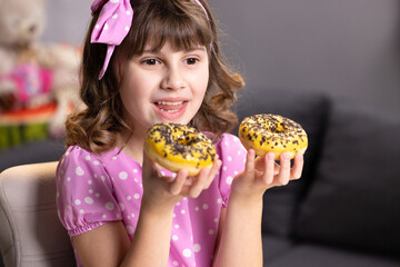 Cheerful school girl playing with cakes indoors. Funny teenager girl having fun with colorful donuts at modern home. Portrait of sweet girl choosing between two donuts in home room.