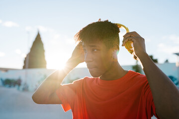 Trendy Latin American guy taking off headphones in city