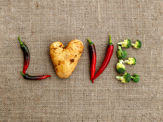 Word Love made of red hot peppers, heart shaped raw potato and broccoli heads on burlap fabric, top view