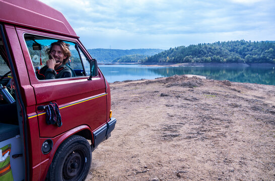 A lonely traveler guy at his window in his camper van in pretty landscapes 