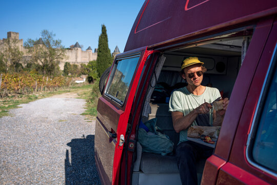 A lonely traveler guy having lunch in camper van by an old castle 