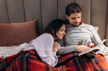 Couple reading book in bed under plaid
