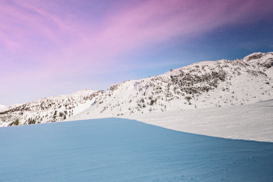 a shadow in the snow with snowy mountains and pink sky
