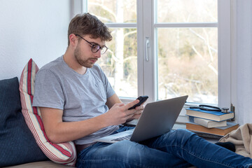 Junger Medizin-Student sitzt beim Lernen zu Hause mit einem Laptop auf seinem Bett vor einem...