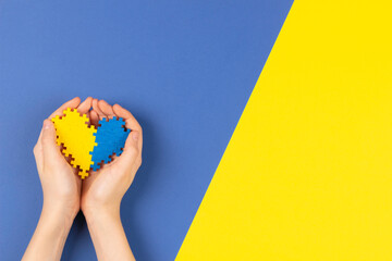 World Down syndrome day background. Child hands holding blue and yellow Down syndrome awareness day heart on yellow and blue background. Top view, copy space