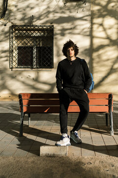 Young man leaning on bench on street