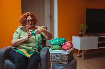 Mature woman holding knitting needles and knitting at home.