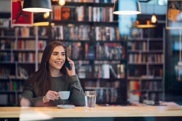 Woman using smartphone and drinking coffee in a cafe.