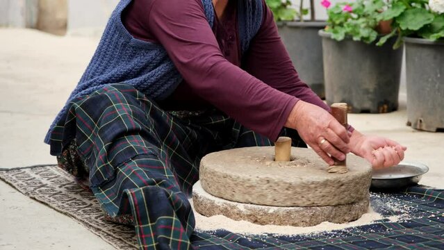 Woman is grinding wheat by hand in stone mill