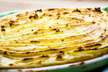 Delicious potato gratin with perfectly baked patterns on the surface, served in an oval ovenproof dish and placed on a bamboo kitchen board.

