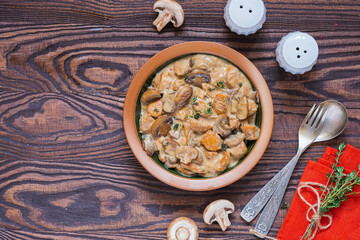 Stewed diced turkey with mushrooms in a creamy sauce in a clay plate on a brown wooden background. Turkey recipes.