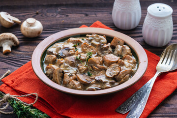 Stewed diced turkey with mushrooms in a creamy sauce in a clay plate on a brown wooden background. Turkey recipes.