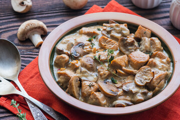 Stewed diced turkey with mushrooms in a creamy sauce in a clay plate on a brown wooden background. Turkey recipes.