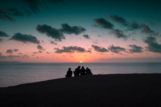 Sitting friends taking pictures at sunset