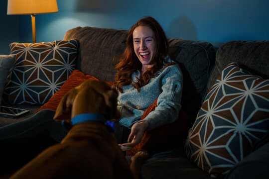 A young white woman relaxes on the couch with her dog