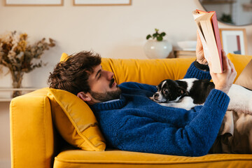Dog resting on owner reading book on couch